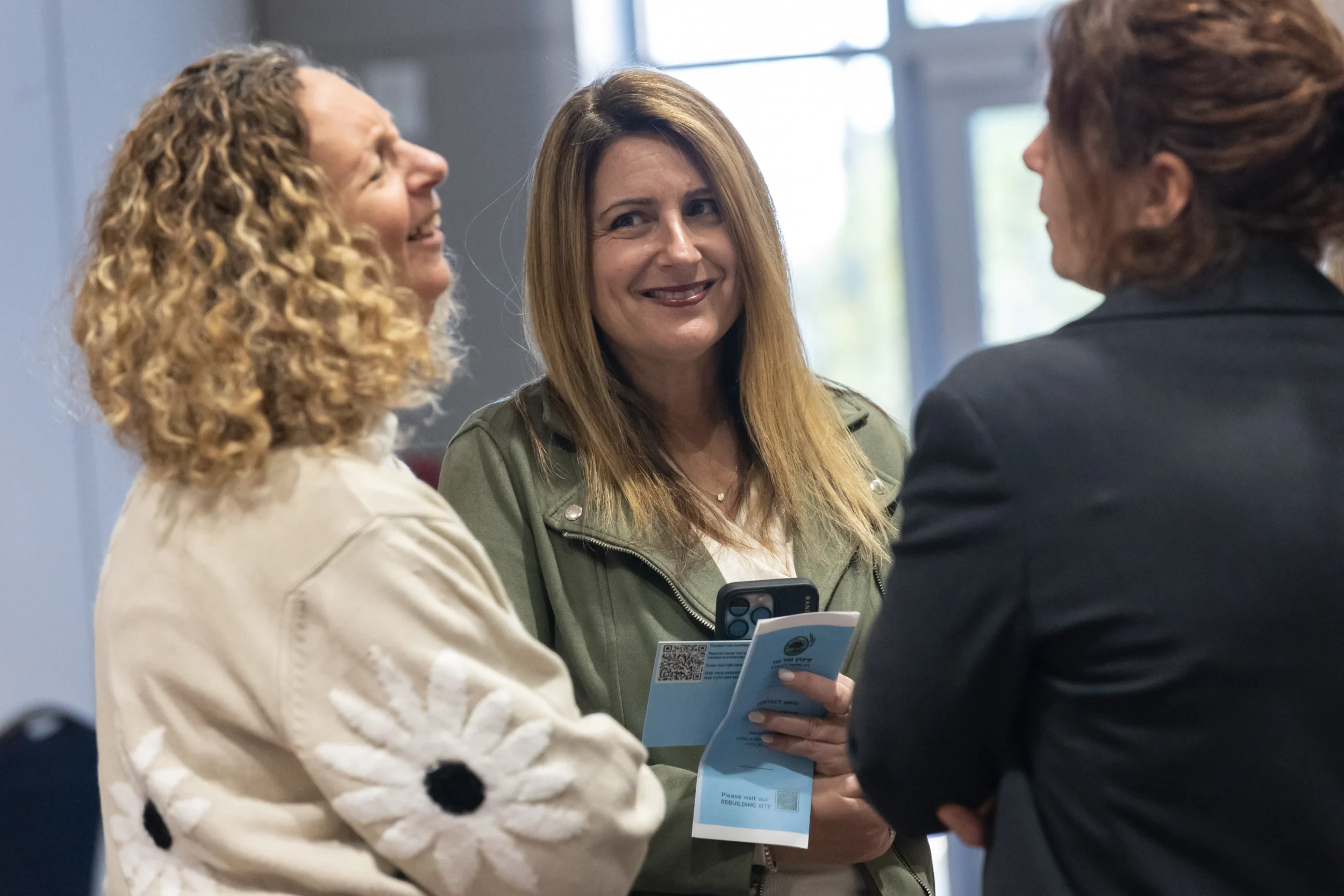Three women stand together in conversation at a Jewish Federation of Greater Atlanta event, smiling and holding event materials during a networking break.