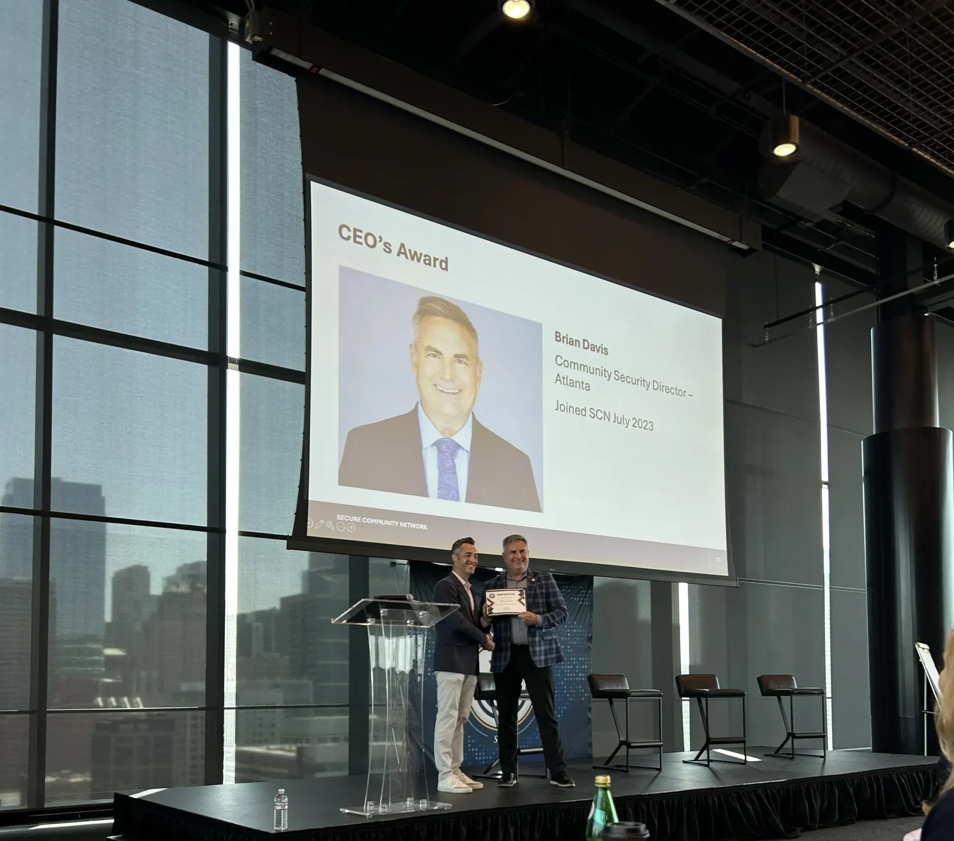 Brian Davis stands on the right holding the SCN CEO Award with another man onstage at the Secure Community Network National Conference.