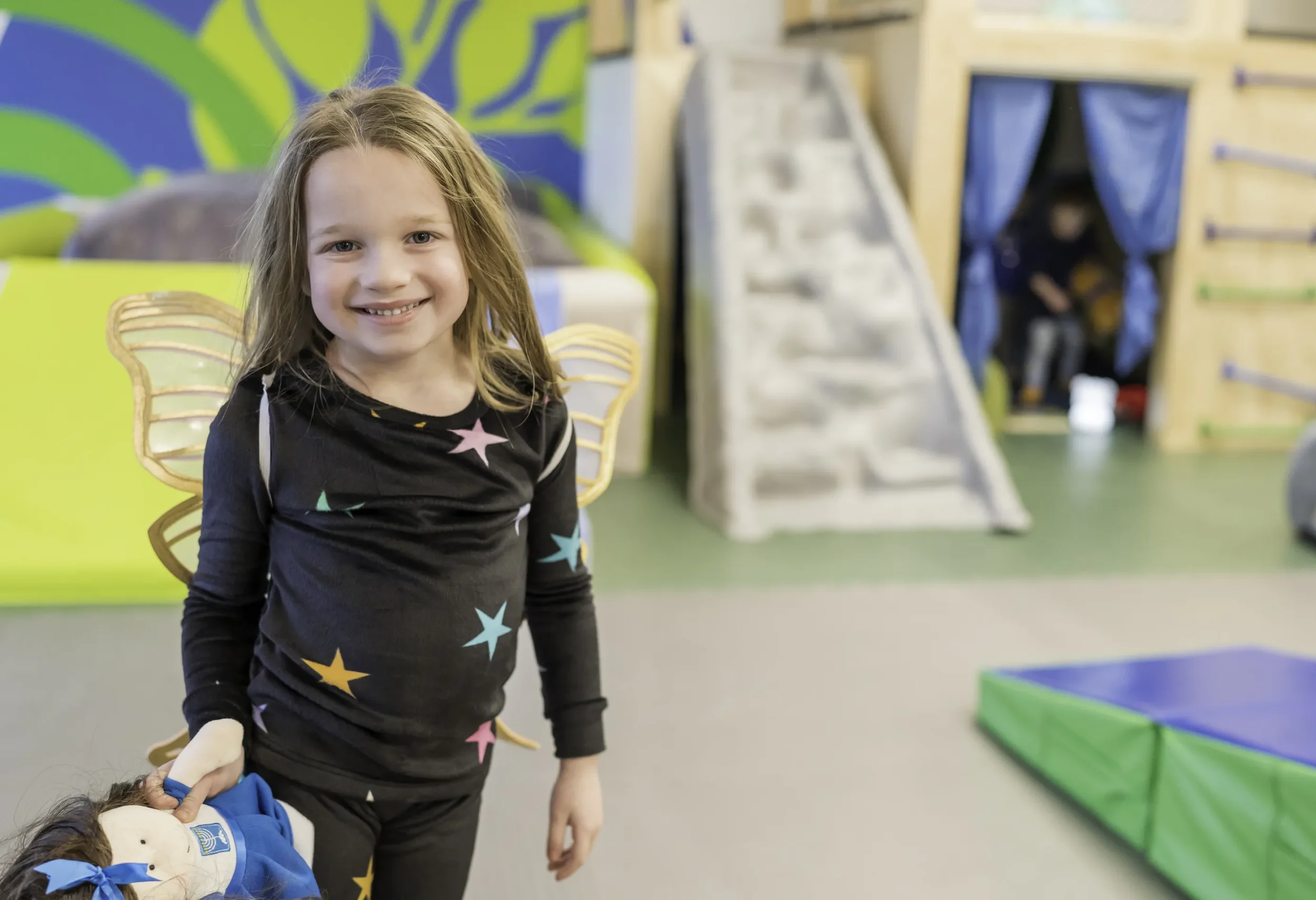 Young girl smiles at camera, wearing pajamas and butterfly wings