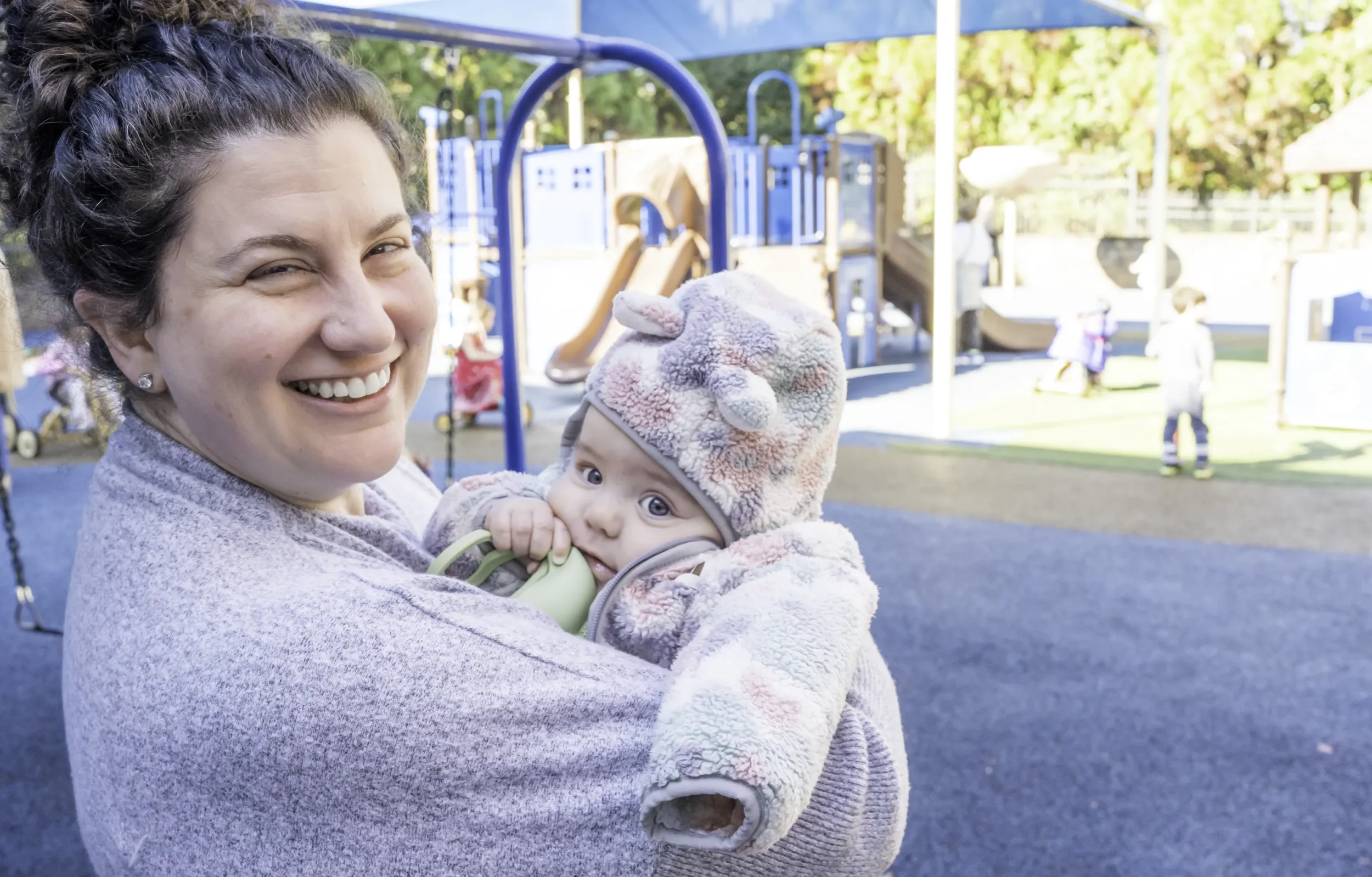 Mom smiling, holding her baby at PJ Event on a Playground