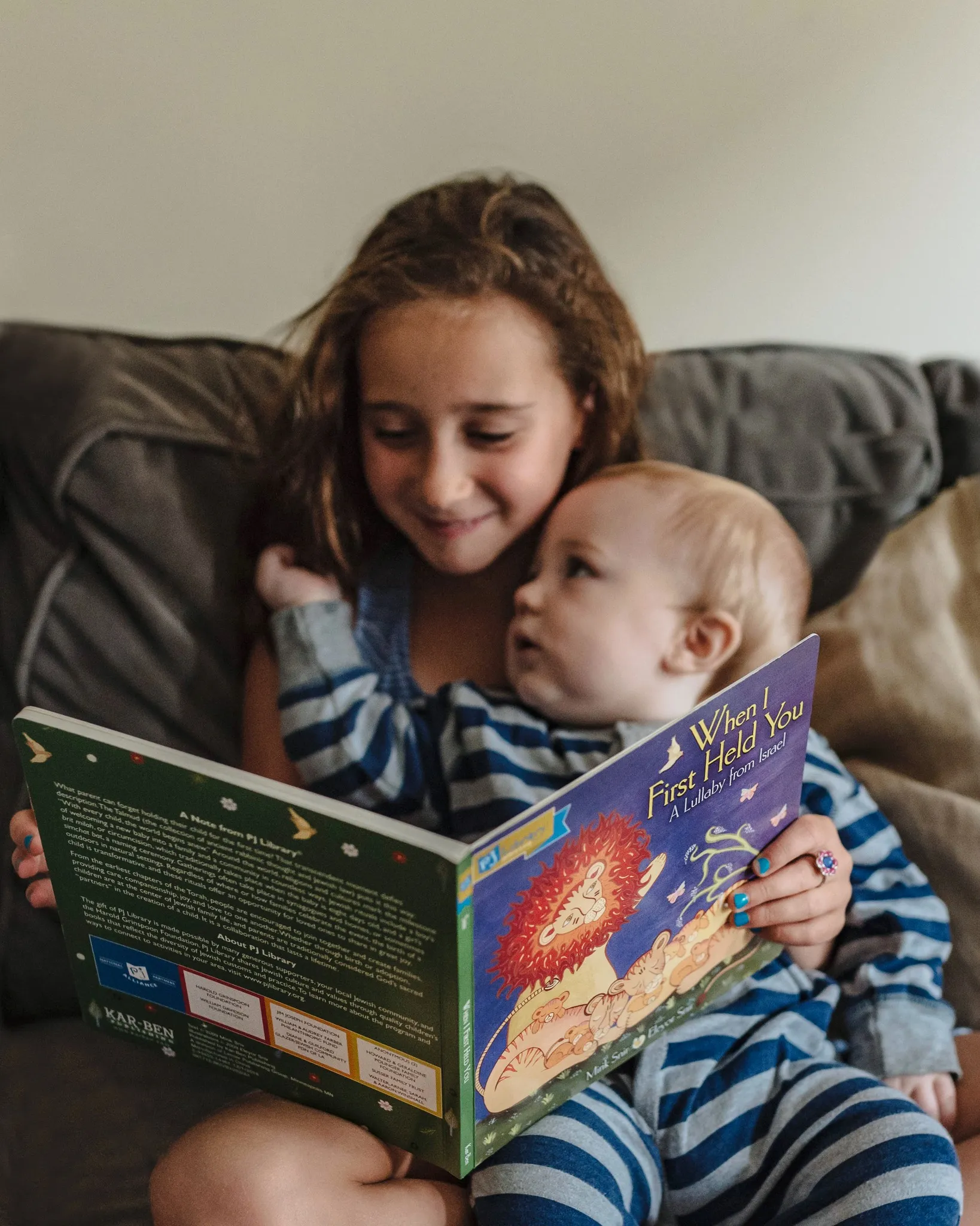 A sister reads a PJ Library book to her baby sibling