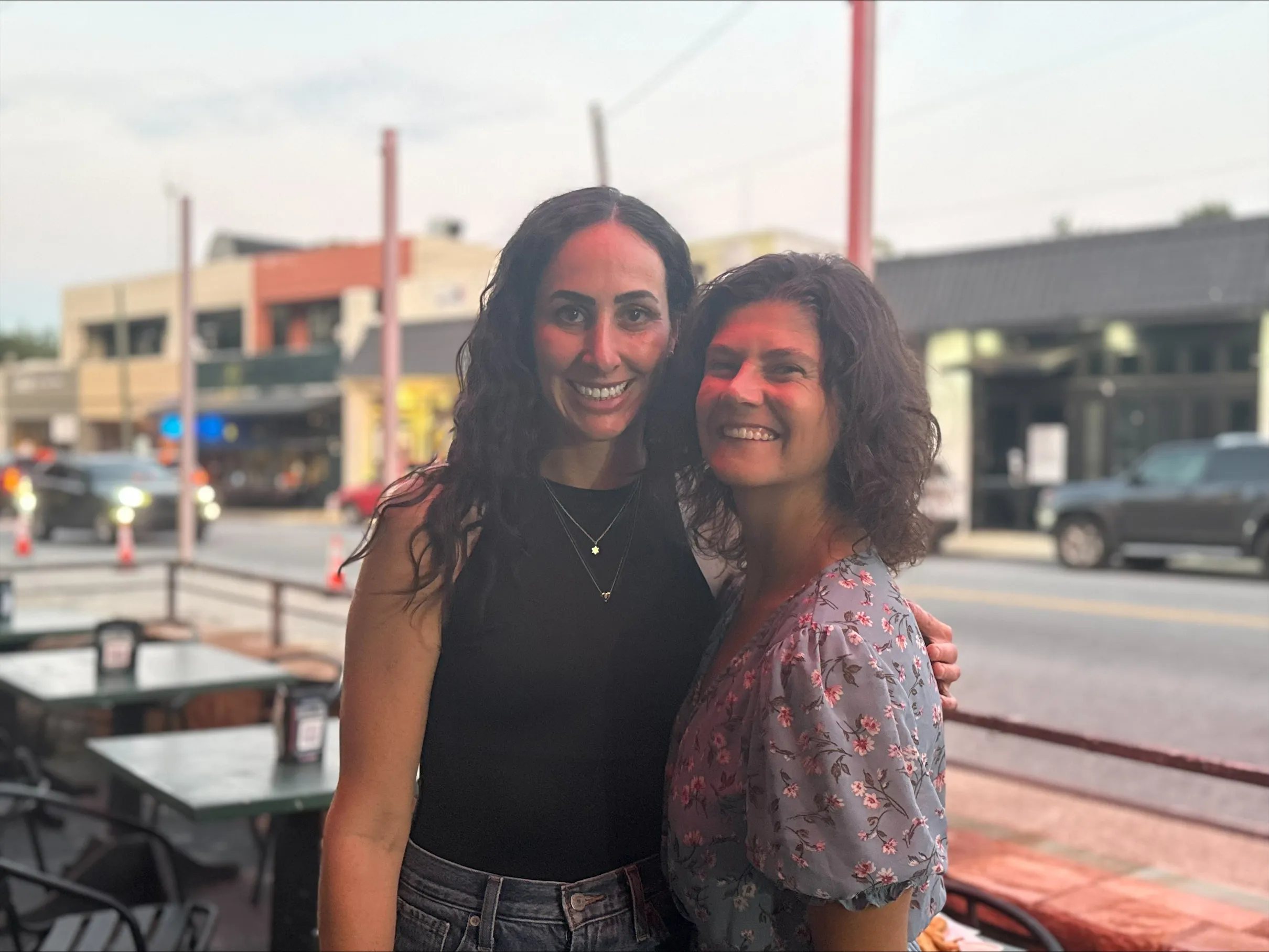 Two women smile together outdoors during a JInterfaith gathering.